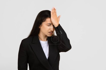 Foto de Mujer de negocios en traje negro que se ve estresada y arrepentida con la mano en la frente como si recordara algo importante que olvidó - Imagen libre de derechos