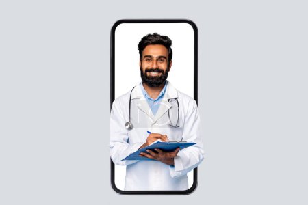 Photo for Smiling middle aged indian male doctor holding clipboard encased within smartphones frame, symbolizing telehealth services, against neutral background - Royalty Free Image