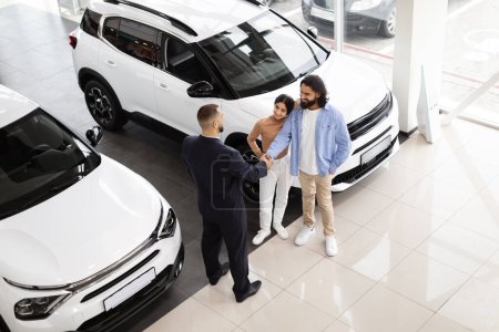 Photo for Top view of young indian man and woman loving couple buying brand new car at luxury auto dealership, eastern customers have conversation with sales manager, shaking hands, successful deal - Royalty Free Image
