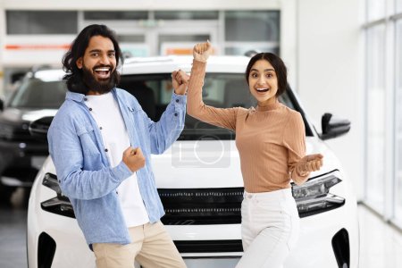 Photo for Overjoyed Indian Couple Celebrating Buying New Car, Dancing In Dealership Office. Happy Eastern Spouses Having Fun In Auto Salon, Emotionally Reacting To Automobile Purchase, Free Space - Royalty Free Image