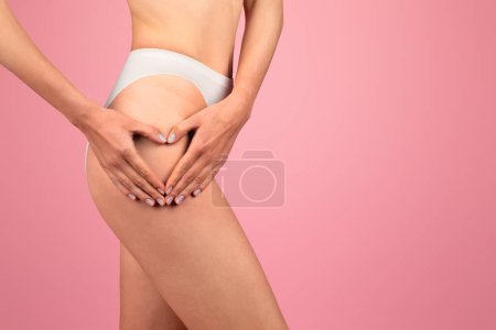 Photo for Close-up of european womans lower back and hips, with her hands forming a heart shape over her buttocks, wearing white underwear, against a gentle pink background, symbolizing body love and health - Royalty Free Image