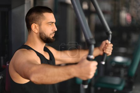 Photo for Portrait Of Motivated Muscular Man Training On Sport Machine At Gym, Young Male Athlete Making Shoulder Press Exercise During Workout In Modern Sport Club, Enjoying Bodybuilding, Closeup Shot - Royalty Free Image