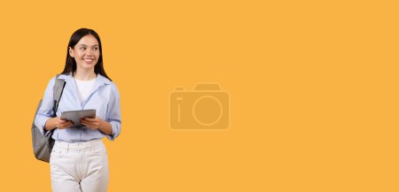 Photo for Smiling female student with backpack holding digital tablet, wearing shirt and backpack, posing against yellow background, perfect for educational content - Royalty Free Image