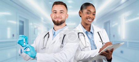 Photo for A european, african american doctor in a white coat preparing a syringe stands next to a smiling female doctor with a clipboard in a hospital corridor, symbolizing teamwork in healthcare - Royalty Free Image