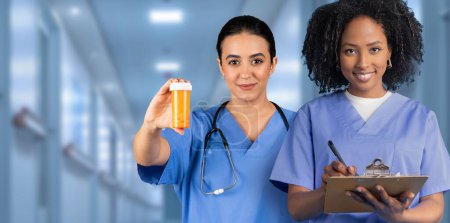 Téléchargez les photos : Deux infirmières attentives en blouse bleue, l'une tenant des médicaments dans une bouteille de pilule orange et l'autre écrivant sur un presse-papiers, représentent des soins diligents aux patients dans un hôpital - en image libre de droit