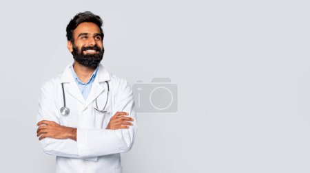 Photo for Optimistic indian bearded male doctor in white coat with stethoscope looking aside at free space with arms crossed, evoking positivity and confidence against light background - Royalty Free Image