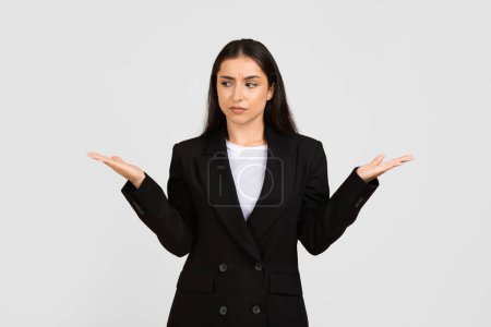 Photo for Professional young businesswoman in smart suit appears uncertain, weighing different options with her hands outstretched in balancing gesture, free space - Royalty Free Image