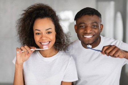 Photo for Portrait of happy married black couple brushing teeth in their bathroom, smiling to camera while doing morning dental care and oral hygiene routine. Shot of young spouses holding toothbrushes - Royalty Free Image