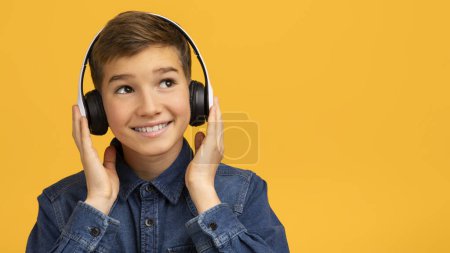 Photo for Portrait Of Smiling Teen Boy Listening Music In Wireless Headphones, Cheerful Teenage Male Child Standing Isolated On Yellow Studio Background, Enjoying Favorite Songs, Panorama With Copy Space - Royalty Free Image