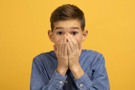 Photo for Teenage boy with shocked expression covering his mouth with both hands, surprised teen male kid standing against bright yellow background, portraying reaction of disbelief or amazement - Royalty Free Image