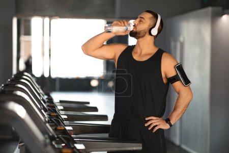 Photo for Handsome Young Male Athlete Drinking Water While Training At Treadmill At Gym, Athletic Muscular Man Having Break During Cardio Workout At Modern Sport Club, Enjoying Jogging, Free Space - Royalty Free Image