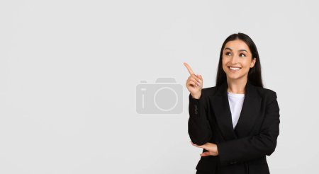 Photo for Confident and smiling businesswoman in professional black suit pointing upwards at free space, perfect for advertisements, isolated on grey background, panorama - Royalty Free Image