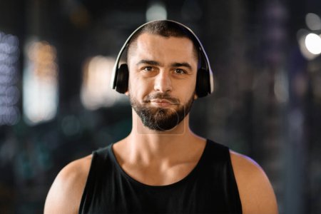 Photo for Portrait Of Smiling Athletic Young Man Wearing Wireless Headphones Posing In Gym, Handsome Caucasian Male Listening Music While Training In Sport Club, Enjoying Playlist For Workout, Copy Space - Royalty Free Image