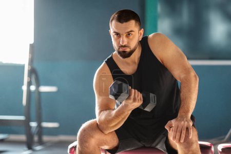 Photo for Motivated Muscular Man Training With Dumbbell In Modern Gym, Strong Caucasian Sportsman Making Seated Biceps Curl, Handsome Male Athlete Working Out With Light Weights In Sport Club, Free Space - Royalty Free Image