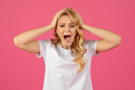 Oh No. Portrait of desperate angry blonde lady screaming looking at camera and touching head, expressing shock over bad news, standing on pink background, studio shot