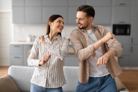 Foto de Jóvenes cónyuges en ropa casual bailando y disfrutando libremente de su tiempo juntos en un ambiente acogedor en casa, mirándose y sonriendo - Imagen libre de derechos