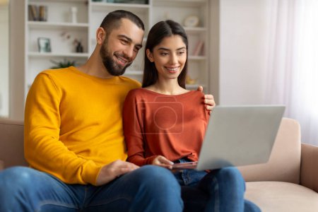 Photo for Portrait Of Happy Young Couple Browsing Internet On Laptop At Home, Joyful Millennial Spouses Resting With Computer In Living Room, Shopping Online Or Watching Photos Together, Free Space - Royalty Free Image