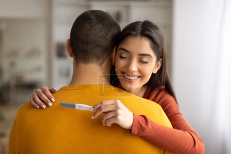 Photo for Closeup of happy young woman holding positive pregnancy test and hugging her husband, millennial family waiting for baby, celebrating becoming parents, enjoying their future parenthood - Royalty Free Image
