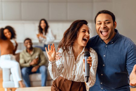 Foto de Diversa pareja se reúne para una alegre sesión de karaoke con un grupo de amigos multiculturales, celebrando su comunidad multiétnica el fin de semana en apartamentos sala de estar. Amistad y entretenimiento - Imagen libre de derechos