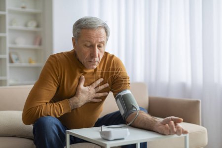 Photo for Hypertension Problem In Senior Age. Shocked Elderly Man Measuring Arterial Blood Pressure Using Sphygmomanometer Cuff Sitting On Couch At Home, Touching His Chest. Healthcare, Health Issue - Royalty Free Image