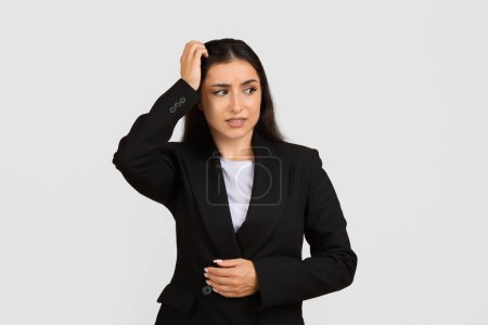 Photo for Pensive professional woman in black suit scratching her head with perplexed expression, symbolizing doubt and confusion in business context - Royalty Free Image
