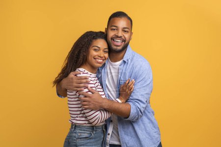 Téléchargez les photos : Aimant couple noir dans une étreinte chaude posant sur fond jaune, heureux jeunes conjoints afro-américains avec des sourires joyeux étreignant et regardant la caméra, debout sur fond de studio ensoleillé - en image libre de droit