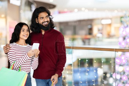 Photo for Loving indian couple checking online promo coupons while shopping together in city mall. Cheerful eastern man hugging his girlfriend, spending time together, purchasing goods, copy space - Royalty Free Image