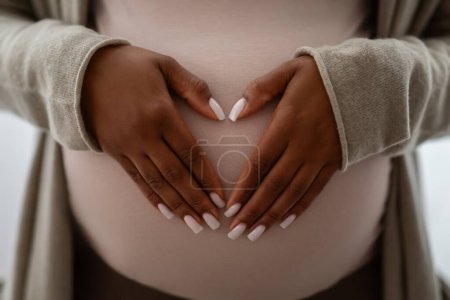 Foto de Maternidad, maternidad, concepto de embarazo. Manos en el corazón en forma de signo en el vientre grande de la mujer embarazada afroamericana. Cortado de esperar a la señora negra abrazando su barriga - Imagen libre de derechos