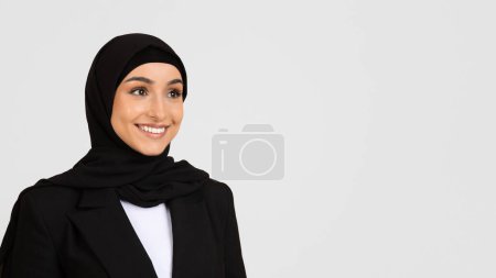 Photo for Radiant young woman wearing hijab and black blazer with beaming smile, standing against light grey background, embodying professionalism, free space - Royalty Free Image