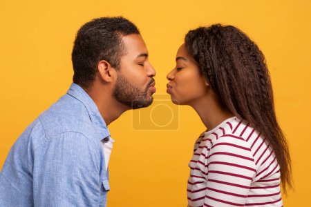 Téléchargez les photos : Vue latérale du jeune couple noir romantique se joignant les uns aux autres avec des lèvres, prêt à embrasser. Amour afro-américain homme et femme exprimant l'amour et l'affection sur fond jaune studio, Gros plan - en image libre de droit
