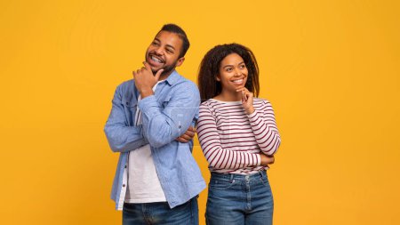 Photo for Portrait of pensive black couple standing against bright yellow background, dreamy young african american man and woman touching chin and looking up at copy space, pondering over ideas, copy space - Royalty Free Image