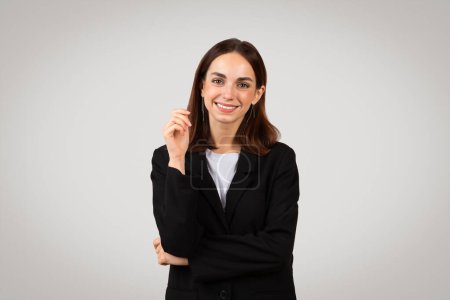 Téléchargez les photos : Femme d'affaires européenne millénaire souriante au regard confiant, pointant le doigt vers le haut comme si elle avait une idée brillante ou présentait une solution, vêtue d'un élégant costume noir - en image libre de droit