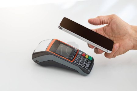 Photo for Hand holding a smartphone above a card payment terminal, indicating a contactless payment process using mobile technology in a white minimalistic setting, cropped. Money services, close up - Royalty Free Image