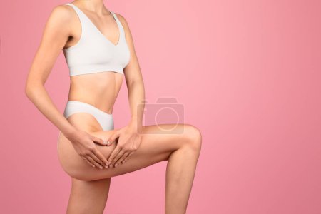 Téléchargez les photos : Une femme caucasienne élancée en tenue de sport blanche tient ses genoux, mettant en valeur sa forme physique et sa santé sur un fond rose dans ce studio tourné, recadré. Bien-être, soin du corps - en image libre de droit