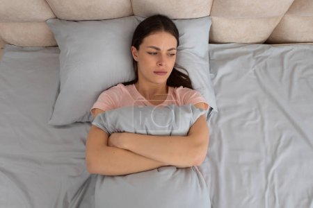 Die beunruhigte junge Frau liegt im Bett, umarmt ihr Kopfkissen, ihr Gesicht geätzt von Sorge und Unbehagen, während sie in der Einsamkeit ihres Schlafzimmers über ihre Gedanken reflektiert.