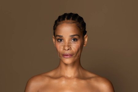 Photo for Portrait of black middle aged woman with natural beauty, elegant natural hairstyle, bare shoulders, exuding tranquility and subtle confidence against brown backdrop - Royalty Free Image