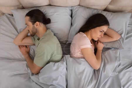 Téléchargez les photos : Couple repose dans le lit avec le dos à l'autre, incarnant l'humeur de tension et de distance émotionnelle, soulignant le moment du problème de la relation, vue de dessus - en image libre de droit