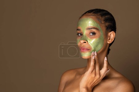 Photo for Serene black middle aged woman with braided hair and reflective expression wearing green facial mask, highlighting spa beauty treatment, free space - Royalty Free Image