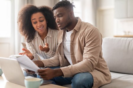 Photo for Couples finance. Young African American spouses, woman and man, handling paperwork sitting near laptop holding bills and offer letters, planning expenses together sitting at home - Royalty Free Image