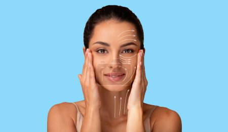 Photo for Facelift Routine. Portrait Of Young Brunette Lady With Lifting Arrows Lines On Face Over Blue Studio Background. Effortless Facial Skincare And Anti Aging Renewal Treatment Concept - Royalty Free Image