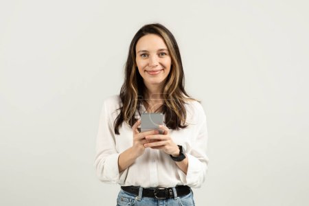 Photo for Content european woman looking at her smartphone, potentially reading a message, dressed in a white blouse and jeans, with a smartwatch, conveying connectivity and technology - Royalty Free Image