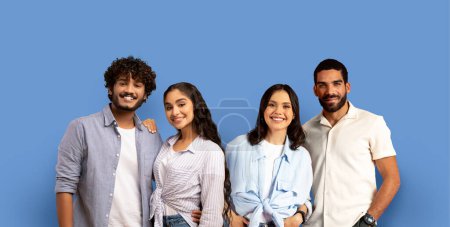 Foto de Cuatro jóvenes estudiantes del milenio en ropa casual de moda con sonrisas radiantes posando para una foto de grupo amigable sobre un fondo azul fresco sólido, panorama, estudio. Estudio, educación - Imagen libre de derechos