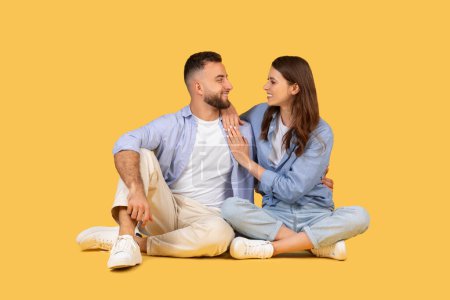 Photo for Happy man and woman sit cross-legged, facing each other in casual attire, sharing tender, joyous moment with warm embrace and loving gazes - Royalty Free Image