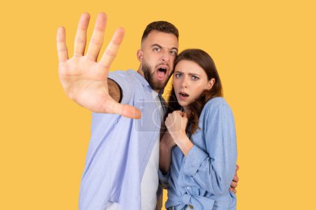 Photo for Startled man and anxious woman, gesturing stop, guy reaching out as if to halt something alarming, be afraid and refuse, posing against yellow backdrop - Royalty Free Image