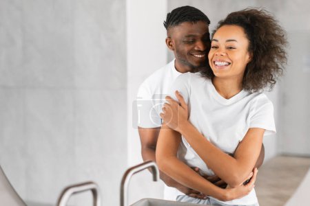Photo for Happy married African American couple shares embrace during morning routine indoor, hugging and smiling in bathroom. Spouses showcasing love in everyday life. Family wellness. Empty space - Royalty Free Image