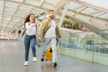 Téléchargez les photos : Jeune couple pressé de courir avec une valise jaune à l'aéroport, heureux homme et femme millénaires riant et profitant du début de leurs vacances, se précipitant à l'embarquement, copier l'espace - en image libre de droit