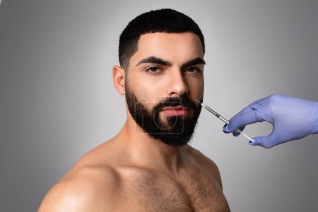 Photo for Attractive bearded man visiting aesthetic clinic, getting smile line filler, closeup. Middle aged shirtless businessman having beauty injection at male spa salon, grey background - Royalty Free Image