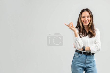 Photo for A smiling european young manager woman with brown hair and a white blouse gestures with one hand, displaying a friendly and inviting expression on a clean background, studio - Royalty Free Image