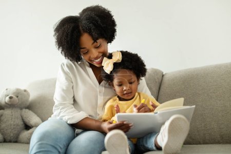 Foto de Desarrollo de niños. Feliz joven madre afroamericana soltera pasar tiempo con su linda hija pequeña en casa, sentado en el sofá y dibujar en el bloc de notas, espacio de copia. Concepto de maternidad - Imagen libre de derechos