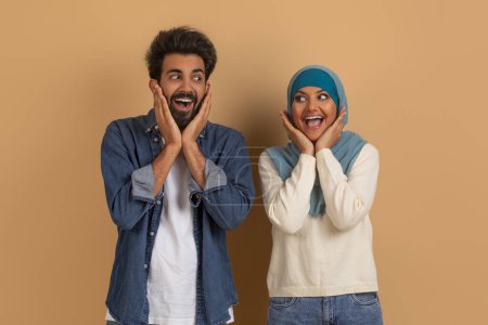 Téléchargez les photos : Super affaire. Portrait de épouses musulmanes étonnantes se regardant et touchant le visage avec excitation, Surpris jeune couple arabe émotionnel posant sur fond de studio beige, Espace de copie - en image libre de droit